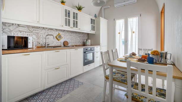 A modern kitchen with white cabinets, a microwave, an oven, and a dining area with a table and chairs. - GuestHost - Beautiful apartment that accommodates up to 4 people, equipped with all the comforts for a pleasant stay, including a furnished sea-view terrace to enjoy unmissable moments of relaxation. The accommodation is located in a period building with (Monopoli)