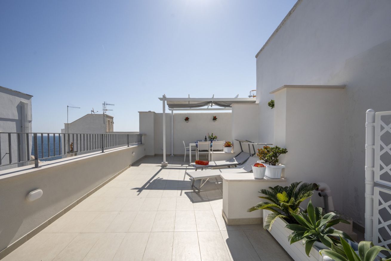 Terraza en la azotea con una pérgola blanca, zona de estar y plantas en macetas.