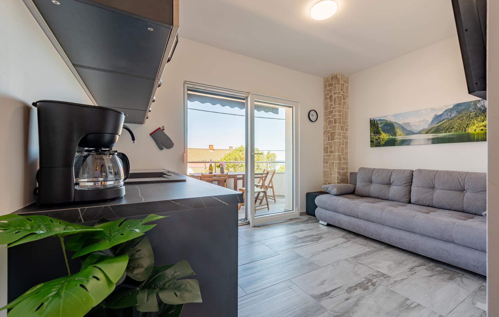 Una cucina moderna con macchina da caffè, zona pranzo con tavolo e sedie, un divano grigio e un'ampia finestra con vista sulle montagne.