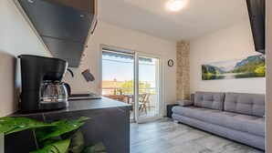 Une cuisine moderne équipée d’une machine à café, un coin repas avec une table et des chaises, un canapé gris et une grande fenêtre donnant sur la montagne.