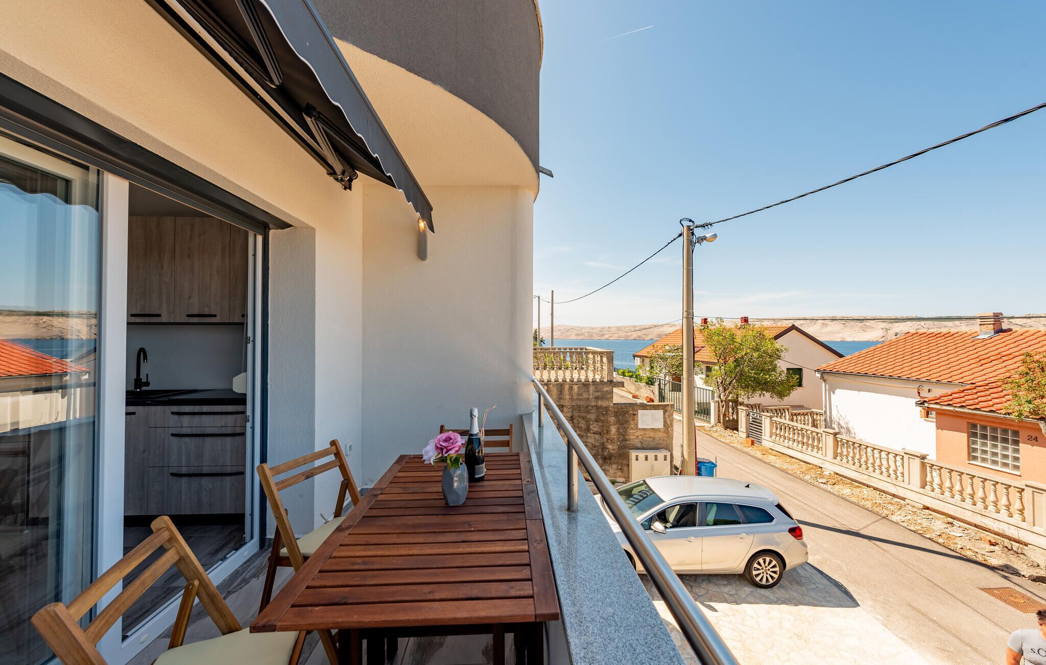 Een balkon met een houten tafel, stoelen en een bloevas. Een auto staat geparkeerd op de straat eronder.