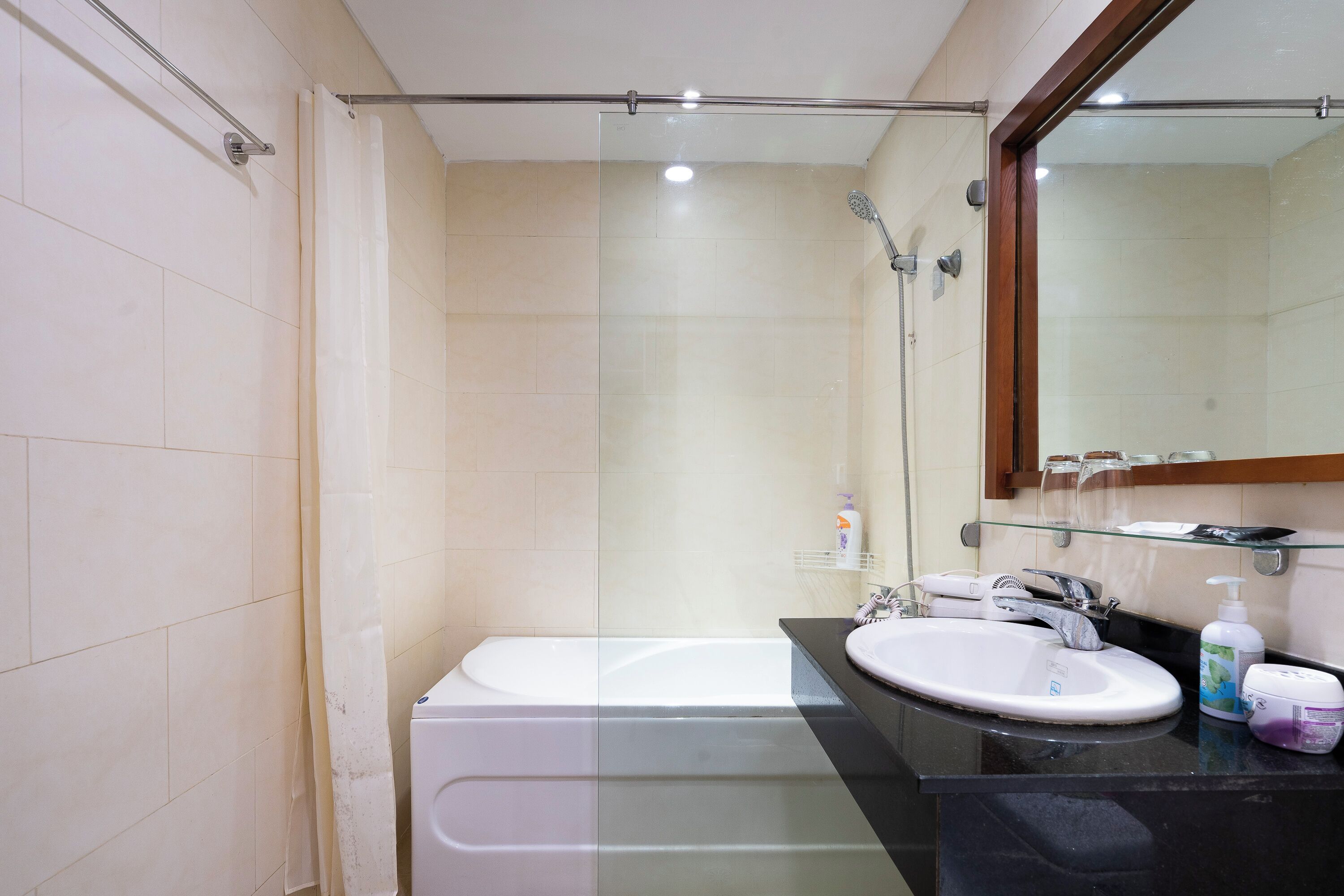 A modern bathroom with a glass shower enclosure, a white bathtub, and a black countertop with a sink and toiletries.
