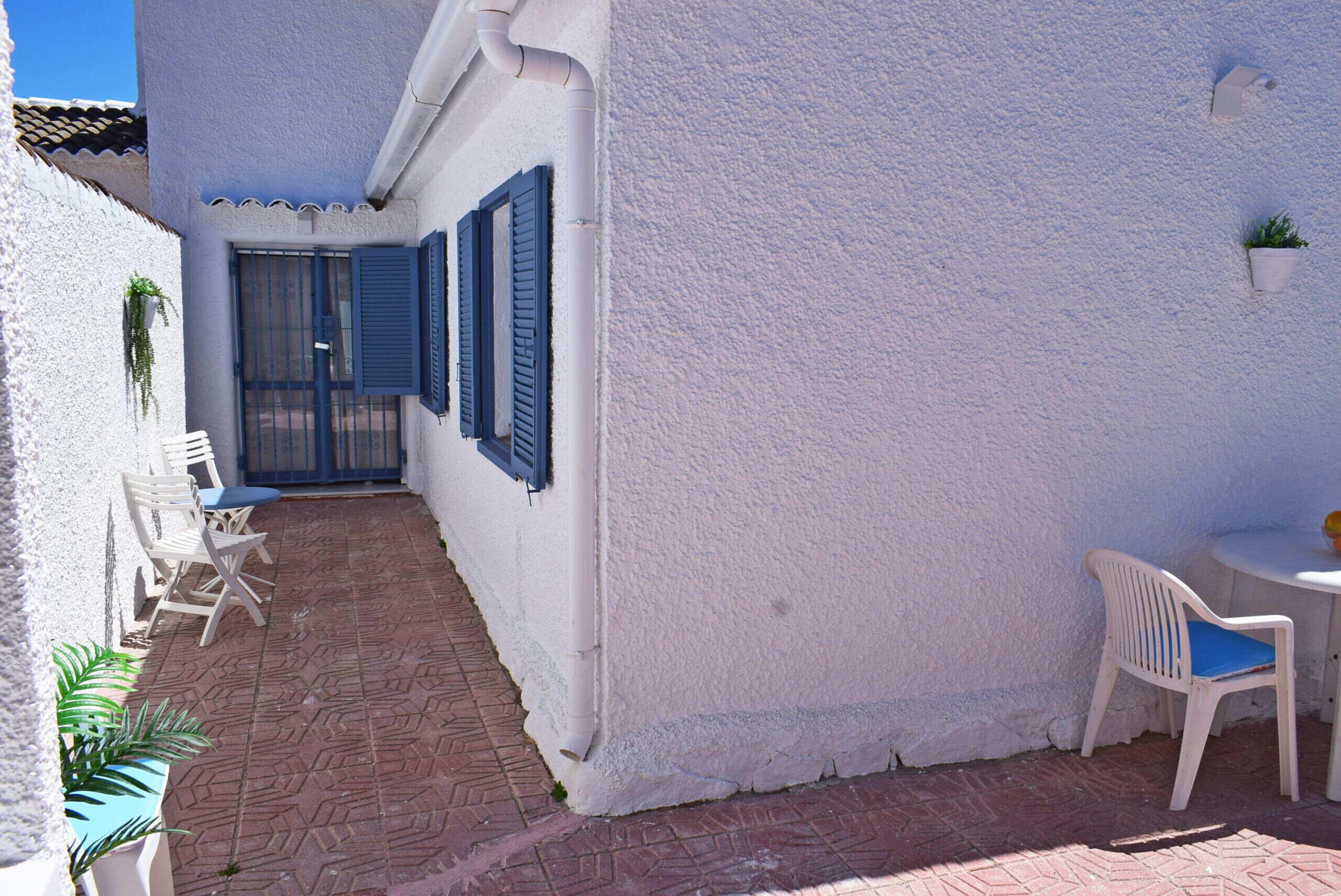 A white building with blue shutters, a tiled patio, and outdoor seating.
