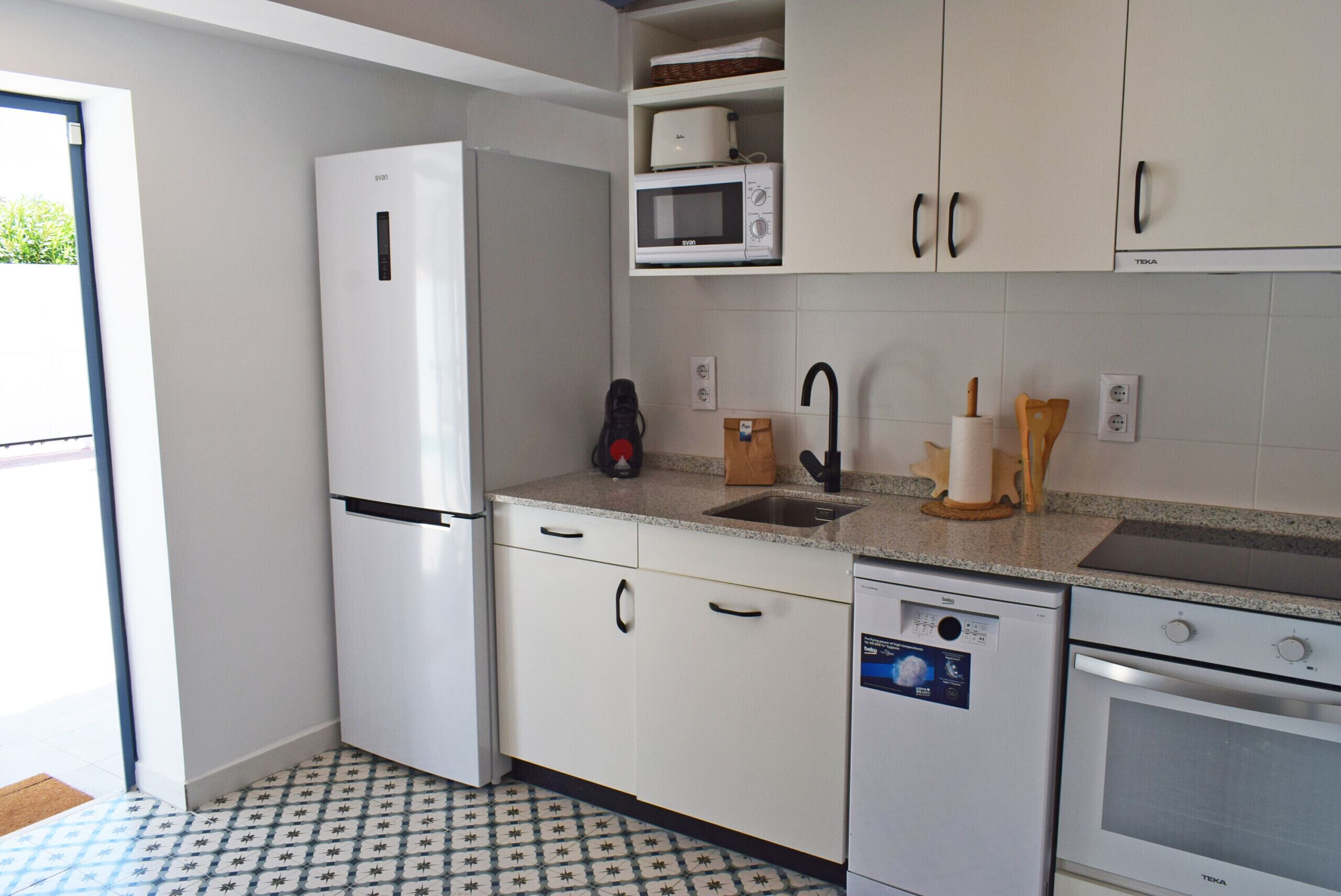 Une cuisine moderne avec des meubles blancs, un four à micro-ondes encastré, un lave-vaisselle et un four traditionnel.