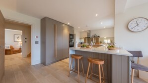 A modern kitchen with a central island, wooden stools, and a clock on the wall.