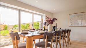A dining area with a large table, multiple chairs, and a view of the garden through large windows.