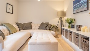 A modern living room with a sectional sofa, a standing lamp, a framed artwork, and wicker baskets on shelves.