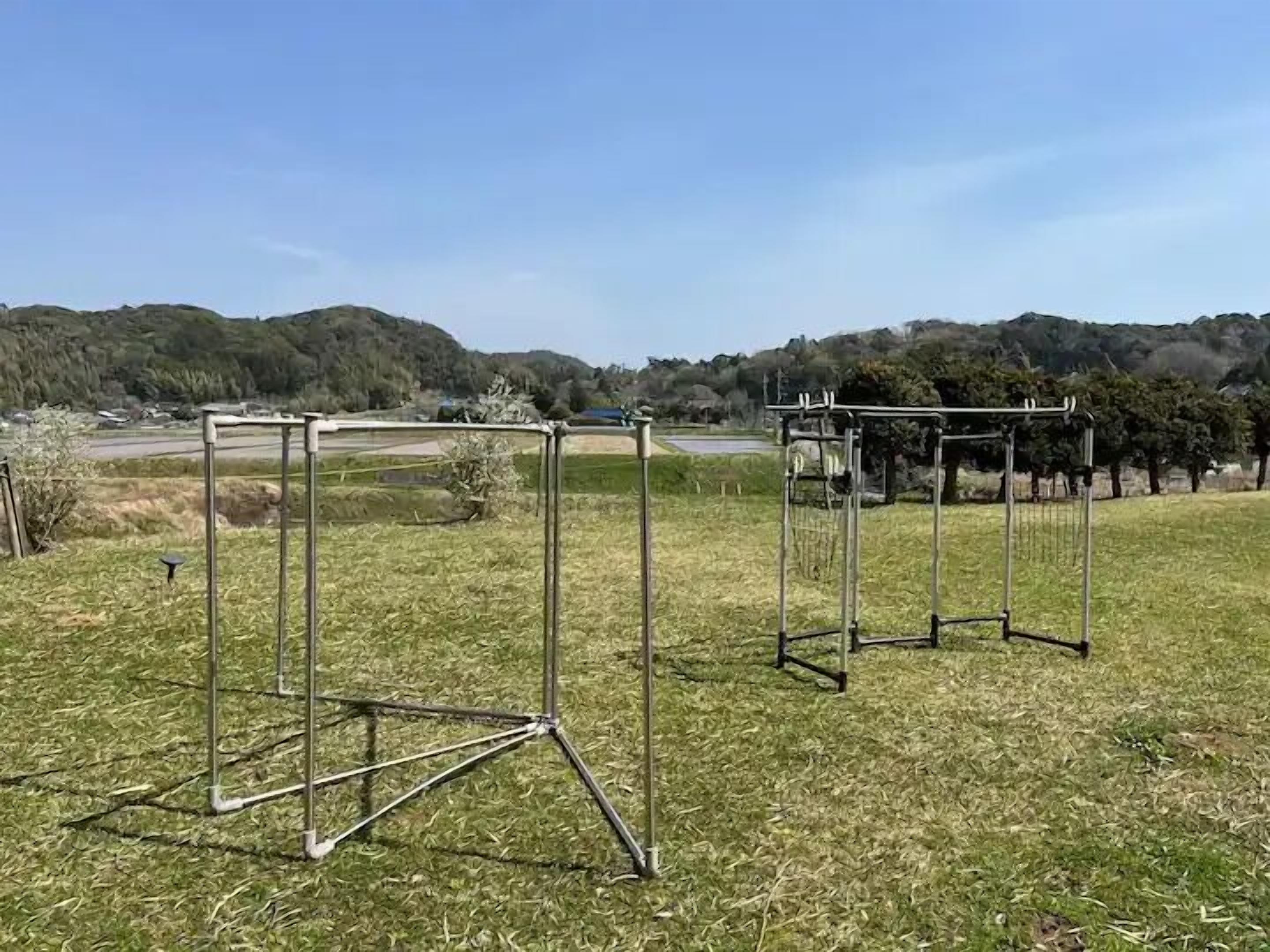 Two metal structures in an open field with a hilly landscape in the background.