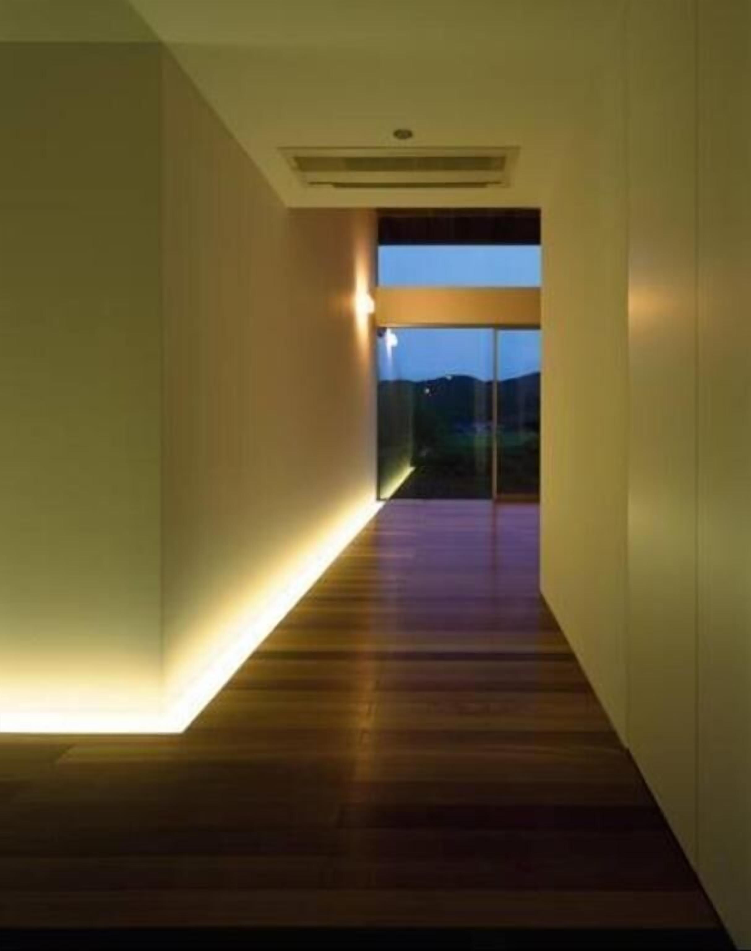 A narrow hallway with a wooden floor and a light source on the left.