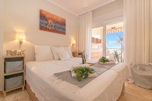 Ein Schlafzimmer mit Bett, Nachttischlampen, einem Nachttisch, einem Fenster mit Vorhängen, einem Balkon und einem Gemälde.
