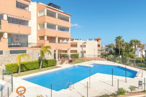 A swimming pool surrounded by a fence, with a stone wall and a building with balconies in the background. - Paraiso De Riviera, Mijas Costa, Spain (Mijas Costa)