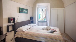 A bedroom with a bed, a window, a radiator, a wardrobe, and a small shelf with a flower. - Casa Felice Sanremo Centre Sea-View Apartment for 4, Sanremo, Italy (Sanremo)