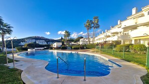 Une piscine à bord incurvé, entourée d’une terrasse en pierre et d’une pelouse.