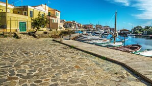 A stone-paved waterfront with boats docked and buildings along the shore. - 1 Le Perle Di Stintino, Stintino, Italy (Stintino)