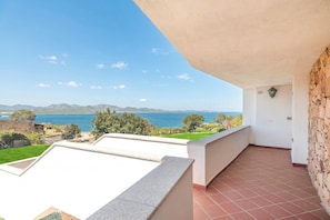 Een balkon met uitzicht op zee en bergen, een betegelde vloer en een stenen muur.