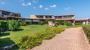 Un patio con un sendero empedrado, una roca grande y un edificio con techo de tejas y balcones.
