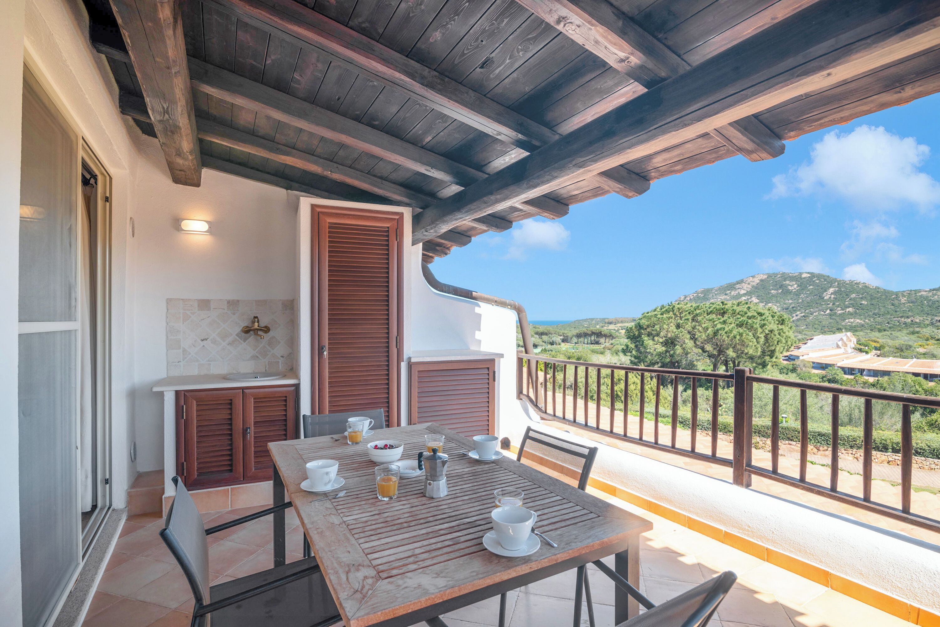 A balcony with a table set for breakfast, a view of the countryside, and a wooden ceiling.
