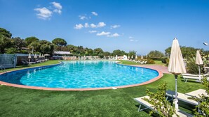 Una piscina con borde rojo, rodeada de césped artificial verde y protegida por sombrillas.