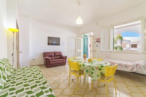 Una habitación con cama, una mesa de comedor con sillas, un sofá, una ventana con vistas y una puerta que da al exterior.