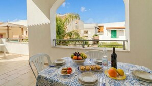 Una mesa de comedor con platos, un cuenco de fruta y una botella de vino, con un cielo despejado de fondo.