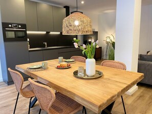 Una cucina moderna con mobili scuri, forno a incasso e zona pranzo con tavolo in legno e sedie in vimini.