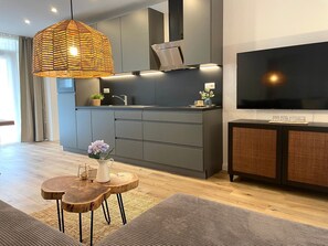 A modern kitchen with grey cabinets, a large TV, and a hanging light fixture.
