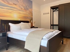 Un dormitorio con cama, mesita de noche, armario y pared con vistas al atardecer.