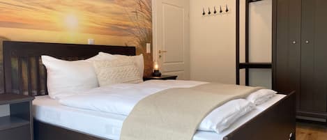 Un dormitorio con cama, mesita de noche, armario y pared con vistas al atardecer.