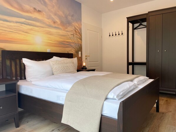 Une chambre à coucher comprenant un lit, une table de chevet, une armoire et un mur donnant sur un paysage au coucher du soleil.
