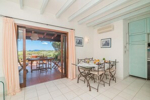 Un comedor con mesa y sillas, vistas a través de un ventanal y una zona de cocina con armarios.