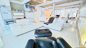 En moderne stue med en hvid sofa, en sort læderfodskanal og en reol fyldt med bøger.