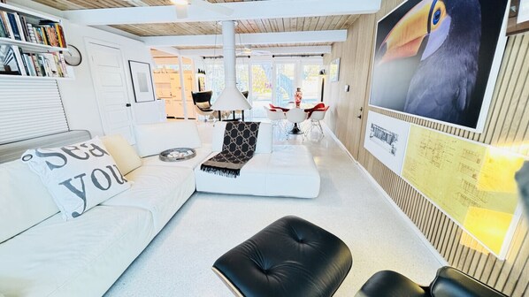 Un salon moderne avec un canapé blanc, un pouf noir et un coin repas avec des chaises rouges.
