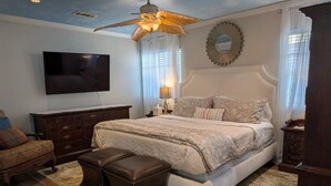 Une chambre à coucher avec un grand lit, un ventilateur de plafond, une télévision, une commode et une table de chevet.