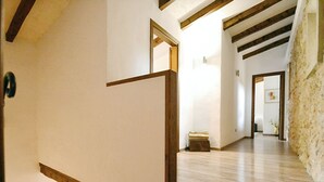 Un escalier en bois, doté d’une rampe, mène à un palier. Le palier est agrémenté d’un mur blanc et d’un plancher en bois. Une porte donne accès à une autre pièce.
