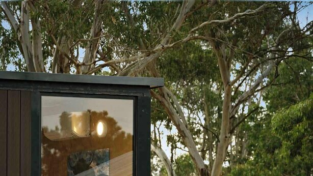 A modern, minimalist treehouse with a bed and a small table, surrounded by natural landscape.
