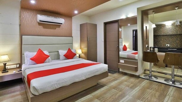 A modern hotel room with a large bed, a mirror, a small kitchenette, and a bathroom. - Presidency Studios (Vadodara)