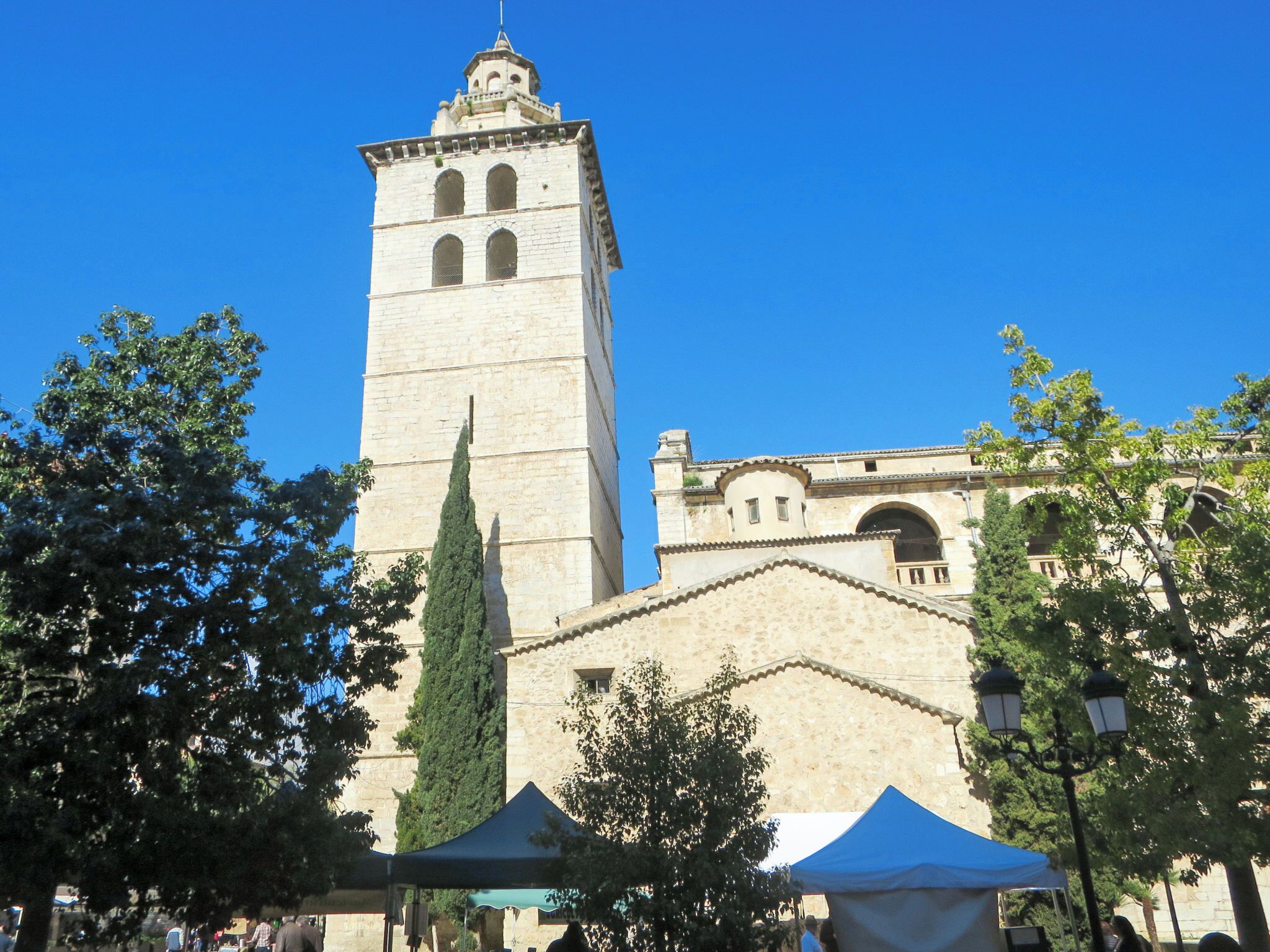 A historic tower with a clock, surrounded by trees and a building with arches.