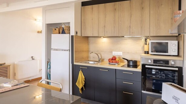 A modern kitchen with dark cabinets, a microwave, an oven, and a sink. - Casa Sémaphore (L'Île-Rousse)