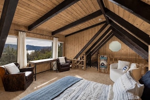 A wooden interior with a bed, two chairs, a desk, and a view of the outdoors.