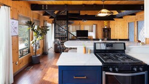 A spacious kitchen with a central island, a dining area, and a staircase leading to an upper level. - Emerald Lake View Loft (Lake Arrowhead)