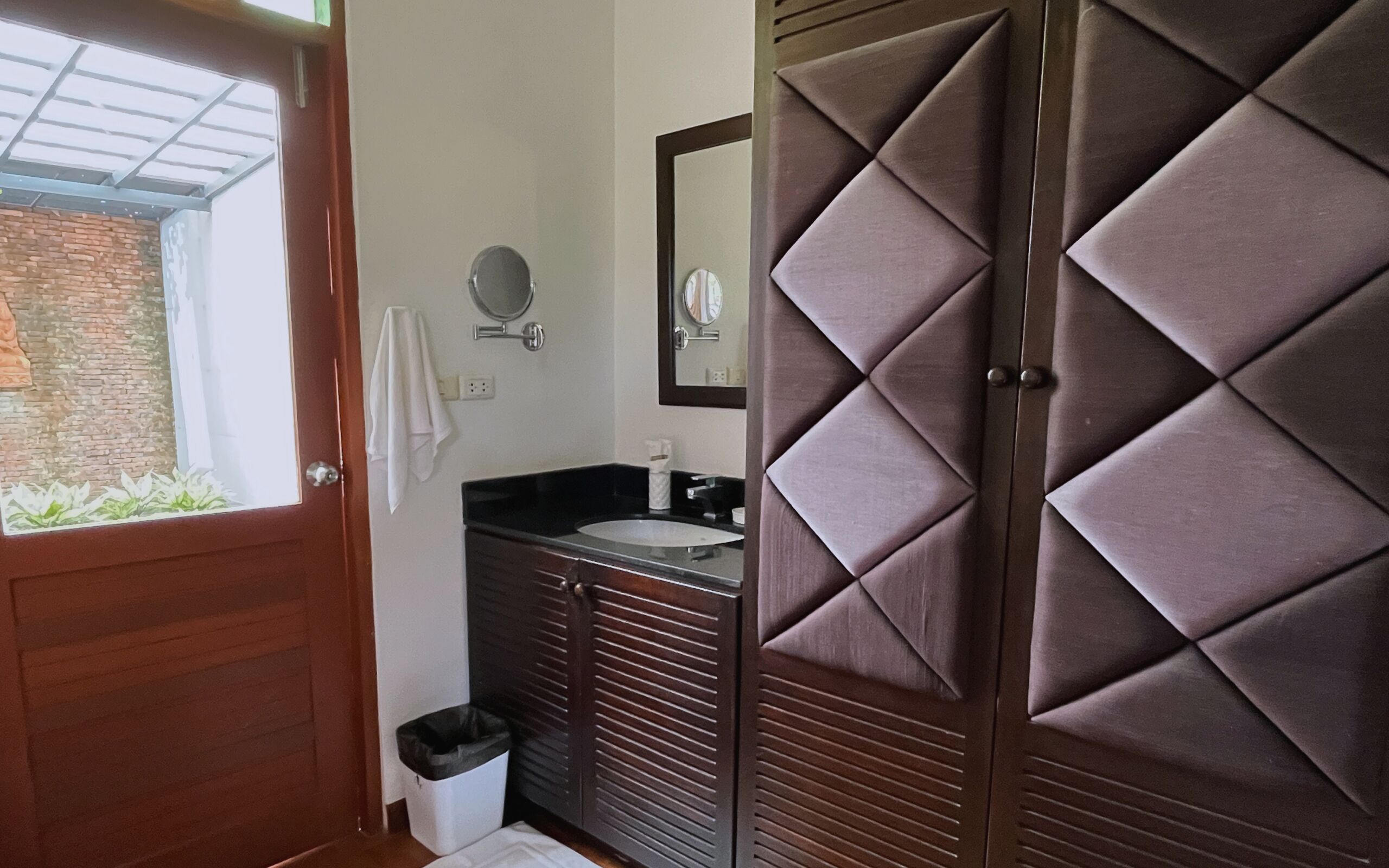 A bathroom with a wooden door, a sink, a mirror, and a towel hanging on the wall.