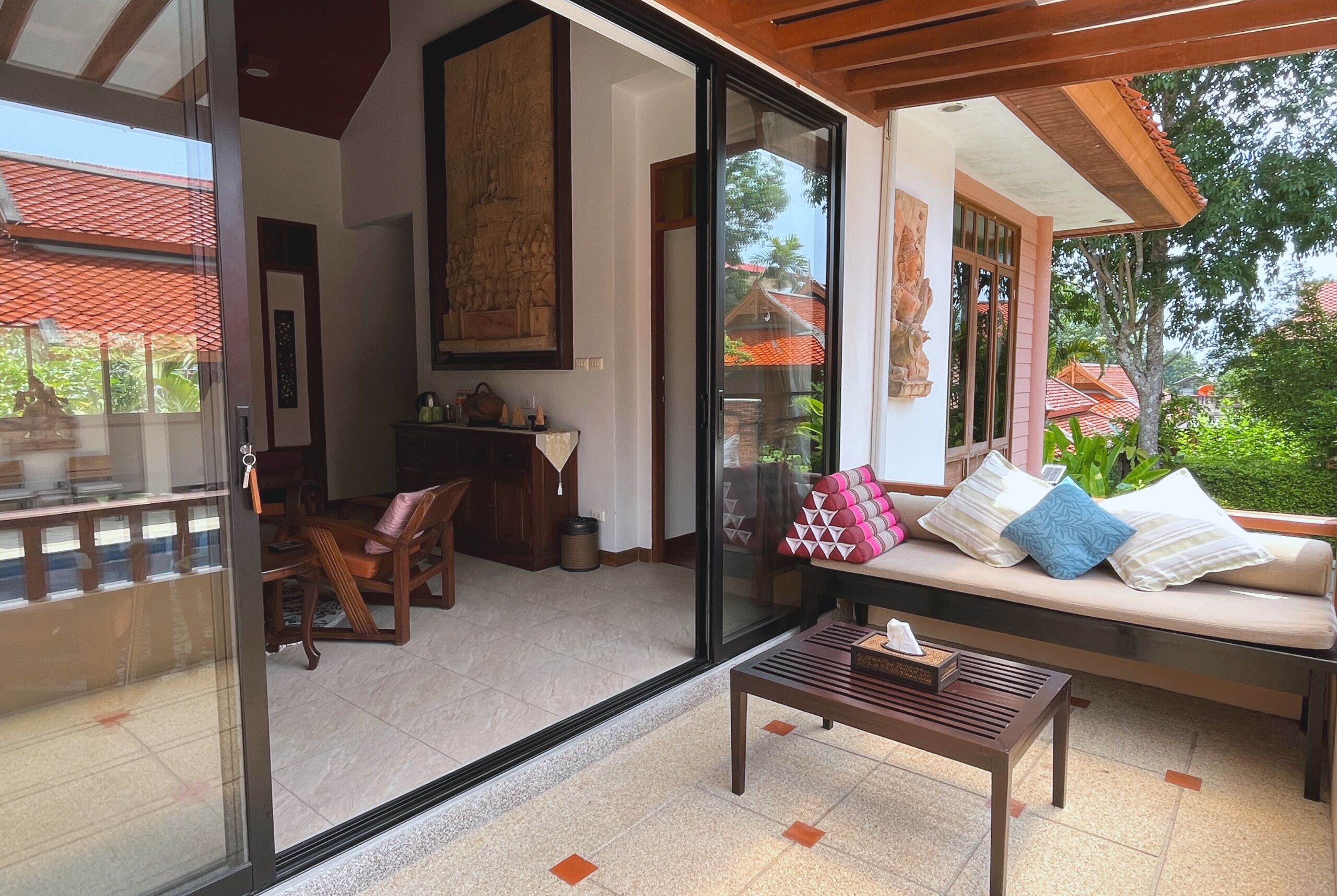 A modern interior with a glass door leading to a balcony, a wooden bench, and a sofa with cushions.