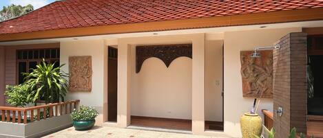 Un edificio con techo de tejas rojas, un vestíbulo cubierto con un arco decorativo y un patio con macetas y plantas.