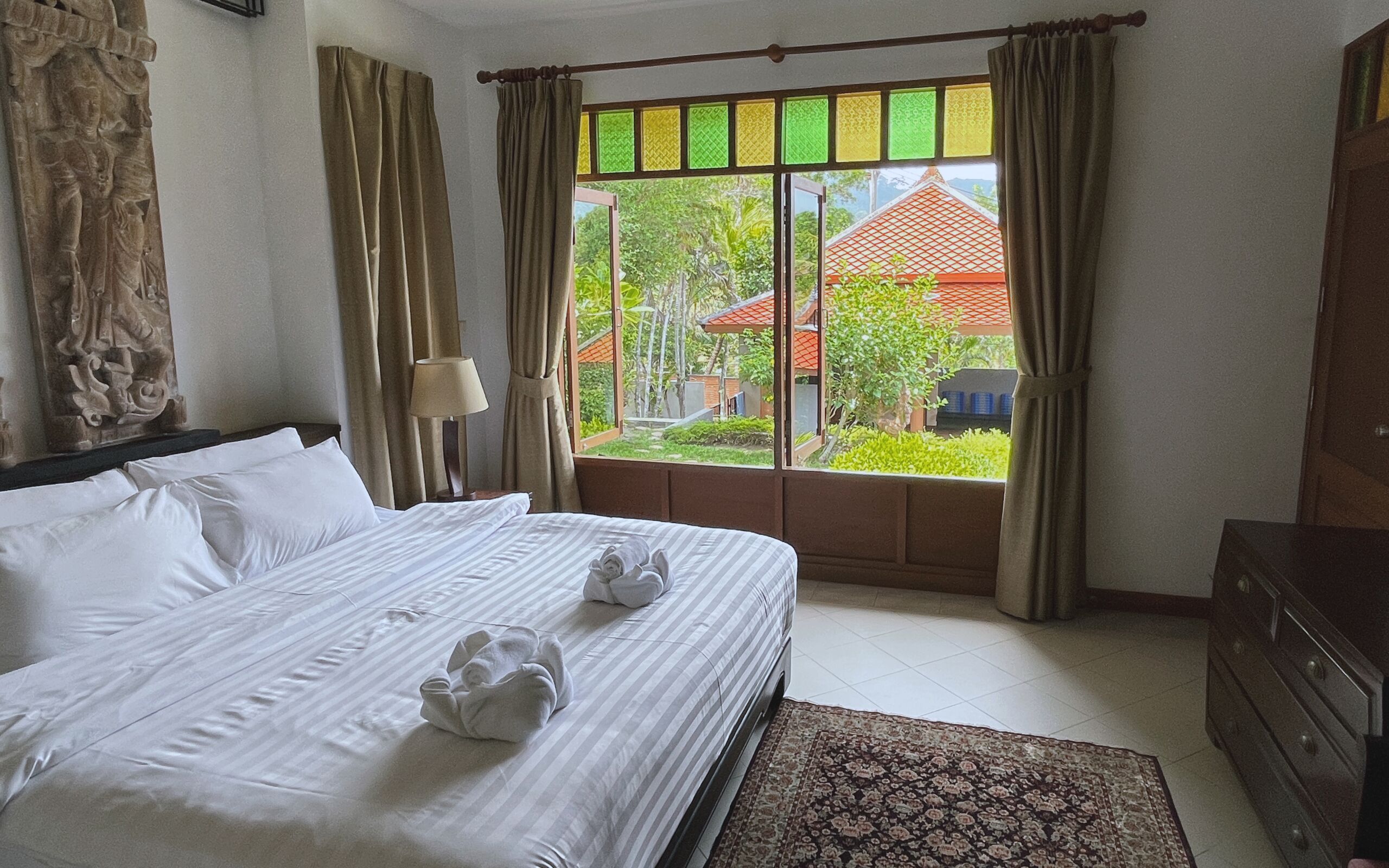Una habitación de hotel con cama, ventana con cortinas, lámpara y cómoda.