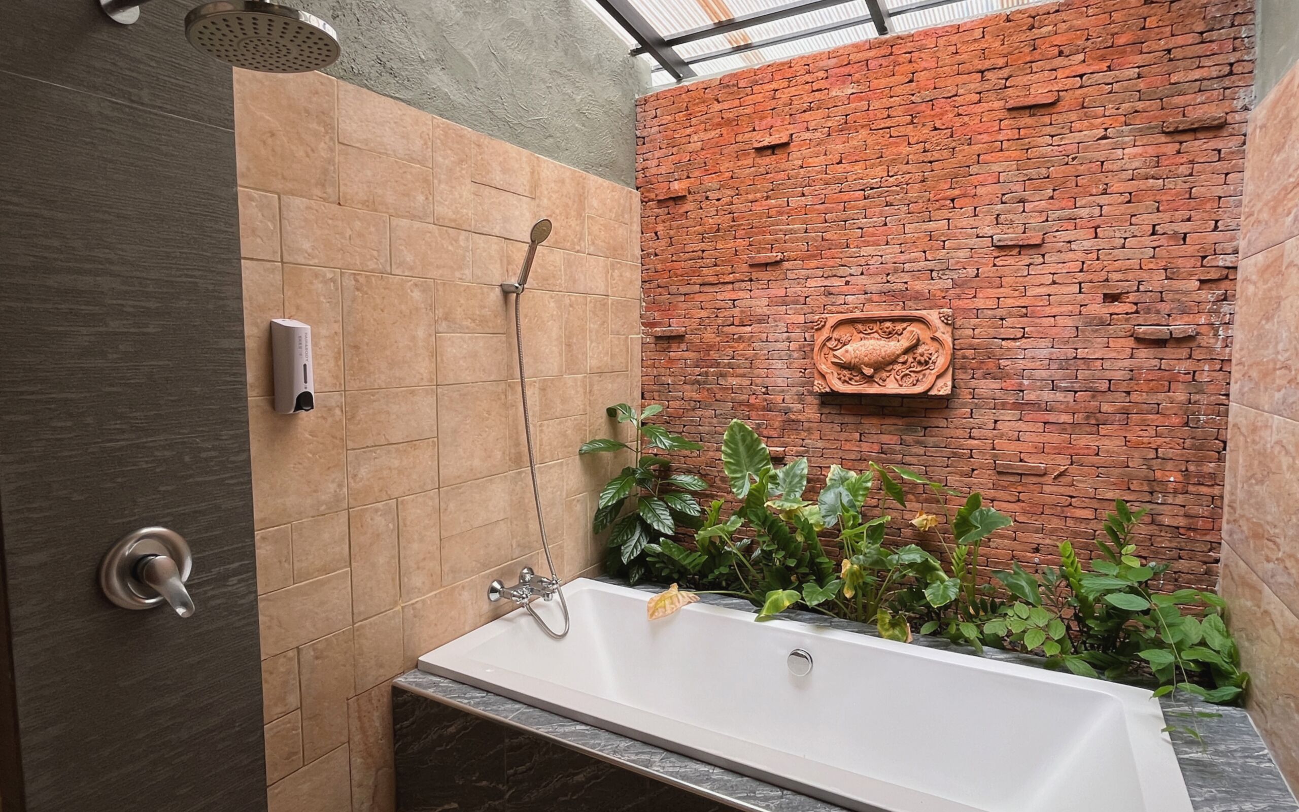 Une salle de bain moderne avec une baignoire, une douche et un mur en briques orné d’une sculpture de poisson.