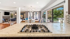 Una cocina moderna con estufa a gas, un comedor con mesa y sillas, y un amplio ventanal corredera que da a un jardín.