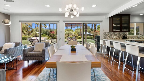 Un comedor amplio con una gran mesa de madera, sillas modernas y vistas a un jardín exuberante a través de puertas de cristal.