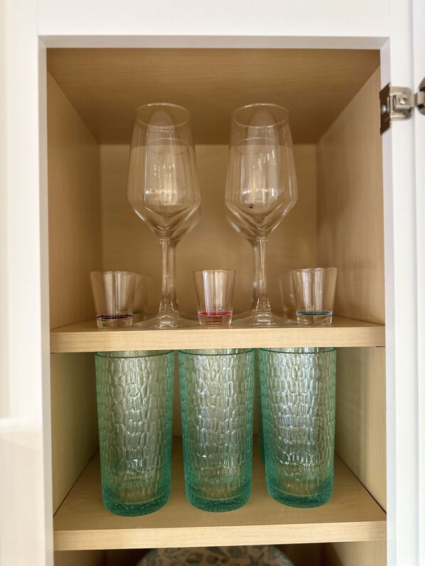 A wooden cabinet with two wine glasses and three glass containers on the top shelf.