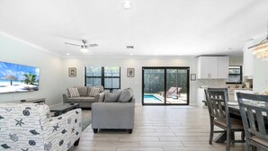 Ein modernes Wohnzimmer mit grauem Sofa, einem gemusterten Hocker, einem Flachbildfernseher und einem Deckenventilator.