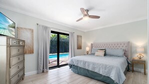 Ein Schlafzimmer mit Bett, Kommode, Deckenventilator und Blick auf ein Schwimmbad.